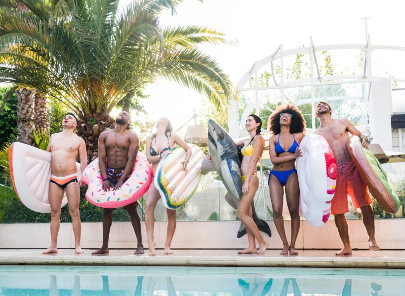 Group of happy friends having fun at pool party with swimwear. Young people vacation at luxury resort hotel