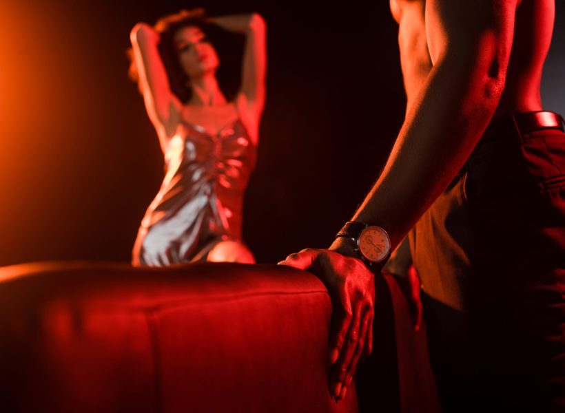 shirtless african american man standing near couch and seductive woman on blurred background