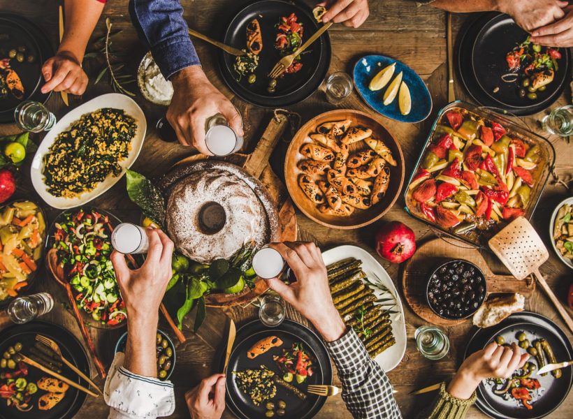 Traditional Turkish celebration dinner. Flat-lay of people eating Turkish salads, cooked vegetables, meze starters, pastries and drinking raki drink, top view, wide composition. Middle Eastern cuisine