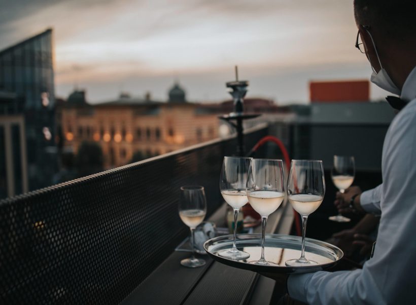 A waiter holding a tray with glasses of white wine on it and serving them to guests at the balcony